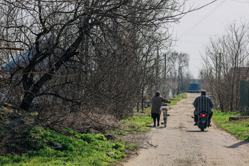 Obraz premium Obukhivka, Dnipro region - 04.11.2021: Man and woman with bicycle and motorbike at typical ukrainian village street, simple coutryside daily life