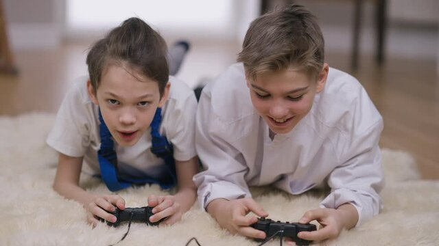 Front view joyful teenage brothers in doctor and builder uniform gaming online laughing talking. Portrait of happy carefree positive Caucasian boys having fun playing video game at home indoors
