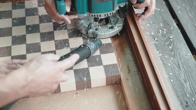 Professional carpenter using grinding machine for carving holes on wooden board made in crafts workshop, artisan joiner creating wooden plank made of two bars of trees sorts. Carpenter sawing wooden
