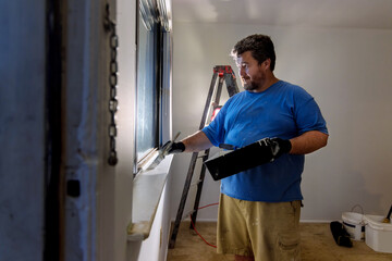 Fototapeta na wymiar Handyman paints a window molding frame with a paint brush