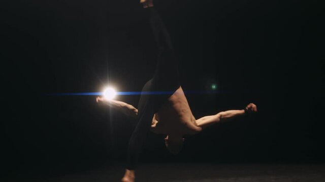 A male athlete is performing acrobatics in gym. Gymnast is jumping and doing flips. Concept of exercises or acrobatic elements and training. Slow motion.