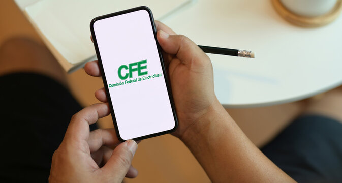 Mano masculina sosteniendo un tel&eacute;fono inteligente con la aplicaci&oacute;n del CFE en la pantalla con un l&aacute;piz en la mano y hojas blancas de fondo. Autlan de Navarro, Jalisco, Mexico. Octubre de 2021