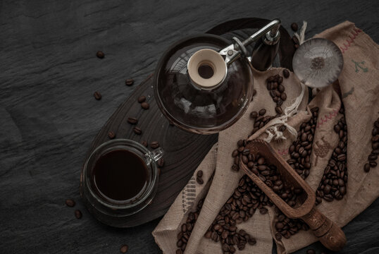 Coffee style, Cup of coffee and coffee beans roating with old wooden scoop and coffee beans around on the wooden and dark stone background. Top view with copy space for your text.
