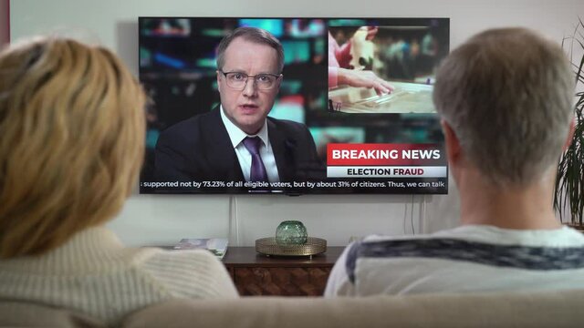 Family Couple Watching TV News Sitting on Couch in Living Room Together. TV Presenter Telling Breaking News about Politics, Elections and Voting Violations