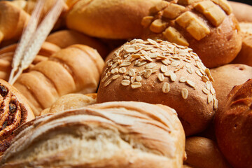 Close up of different types of breads and golden buns with ears of wheat. Food and bakery concept. Salty and sweet food. Bakery and carbohydrates. Horizontal photo.