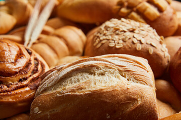 Close up of different types of breads and golden buns with ears of wheat. Food and bakery concept. Salty and sweet food. Bakery and carbohydrates. Horizontal photo.