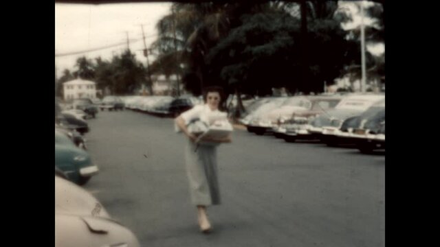 Woman Holding Gifts (1950) - A woman walks down the street holding gifts in her arms.