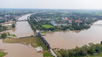 Fototapeta premium Aerial view of Rama 6 Dam (Phra Narai Gate) in Thailand with powerful of water. During Flood disaster in Central of Thailand. Many buildings are submerged in water.