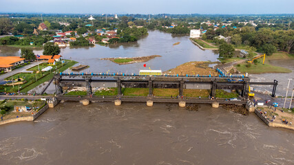 Fototapeta na wymiar Aerial view of Rama 6 Dam (Phra Narai Gate) in Thailand with powerful of water. During Flood disaster in Central of Thailand. Many buildings are submerged in water. 
