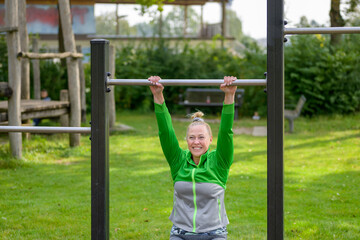 Fit woman having fun working out on bars in a park