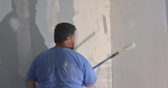 Worker priming with a paint roller with repair the wall after applying plaster for interior reconstruction works