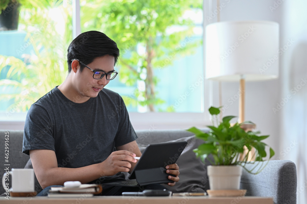 Poster handsome asian man working with computer tablet on sofa.