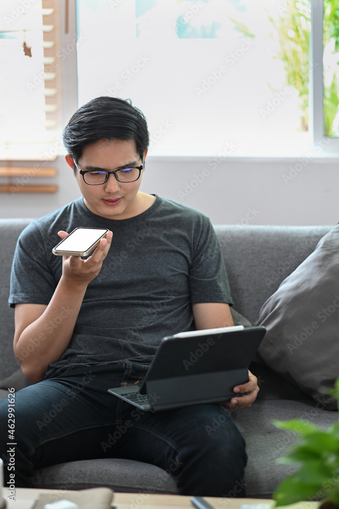 Poster man working with computer tablet and talking on mobile phone in living room.