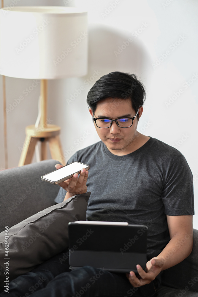 Aufkleber man talking on smart phone and working with computer tablet in living room.