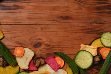 Dried mix vegetables chips with okra, carrots, pumpkin, beetroot and shiitake mushrooms on wooden background. Copy space.