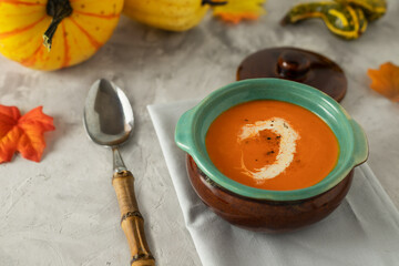 Pumpkin soup in a pot on a concrete table with spoon and pumpkins on the background, horizontal