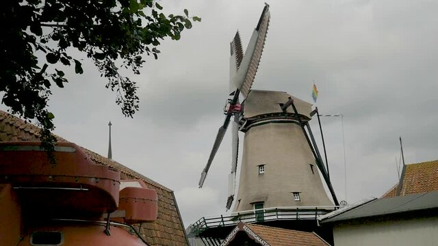 Slow motion Old Dutch windmill spinning in the wind. On the back of the mill we see a rainbow flag. The windmill is part of a museum. Filmed outside museum.