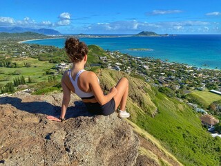 woman on the rocks overlooking the ocean and city - obrazy, fototapety, plakaty