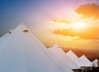 Row of white pyramid tents on high hills for travellers with the sunset background. Soft and selective focus.
