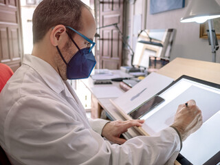 Artist with face mask drawing at the work table in his painting studio. Selective focus