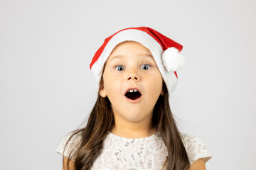 close-up portrait of surprised, shocked, open-mouthed girl in red Santa Claus hat, isolated on white background with copy space. 