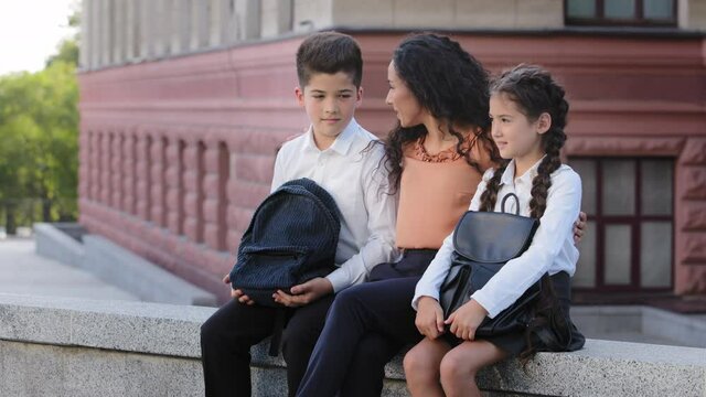 Young Woman Loving Mother Mom Teacher Sits In Schoolyard On Street Outdoors With Children Beloved Daughter And Son Schoolchildren Talk, Hispanic Family Two Students And Mommy Talking After School