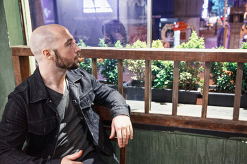 Handsome masculine man dressed casually sitting by a window at night and looking outside. Young...