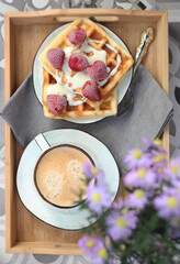 Waffles with cream and strawberries on a tray with coffee