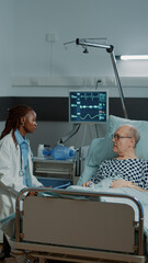 Caucasian nurse checking information files on patient while african american doctor talks to old...