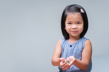 Cute Asian child girl holding coins in her hands. Sweet smiling kid. Happy children playing silver...