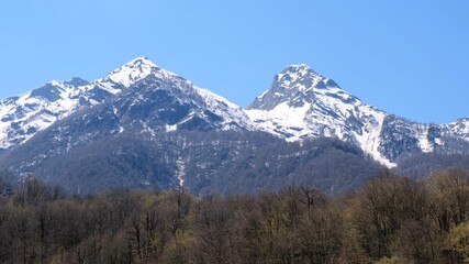 Fototapeta premium picturesque landscape of snow-capped mountains with white clouds on a blue sky on a sunny day at Krasnaya Polyana in Sochi, Russia