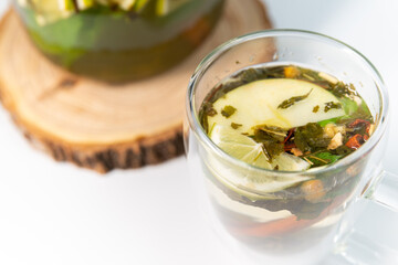 Moroccan tea in a transparent teapot on a white background next to a filled transparent mug close up