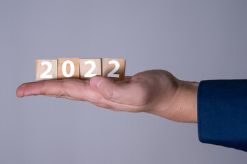Happy New Year 2022 theme men's hands holding wooden cubes with the number 2022 on the palm.