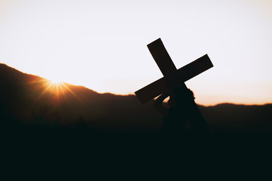Girl with a carrying a cross on his back at sunset, christian silhouette concept.