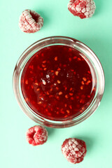 Jar of raspberry jam with ingredients on mint background