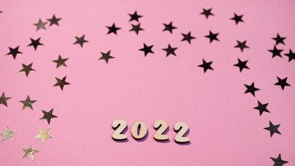 Cheerful wooden lettering happy new year 2022 on a soft gently pink background with gold stars. Sparkle confetti holiday concept 