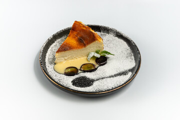 cheesecake on a black round plate powdered with powdered sugar on a white background