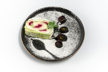 meringue roll on a black round plate powdered with powdered sugar on a white background