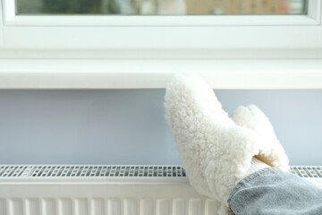 Concept of heating season with legs in knitted boots on radiator