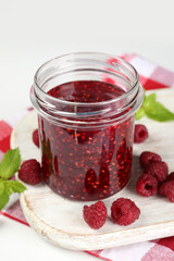 Jar of raspberry jam with ingredients on white wooden stand
