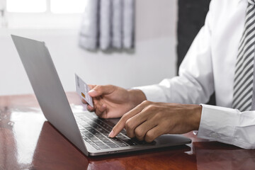The businessman's hand is holding a credit card and using a laptop for online shopping and internet payment