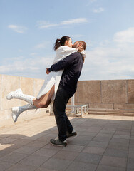 Happy couple celebrating relationship anniversary on building rooftop enjoying tower panoramic view. Caucasian wife and husband hugging at observation point with metropolitan city panorama