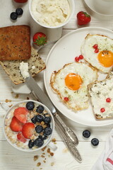 Scrambled eggs with ricotta sandwiches, muesli with milk and fruits on a white plate