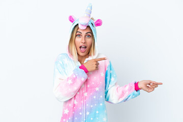 Blonde Uruguayan girl wearing a unicorn pajama isolated on white background surprised and pointing side