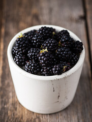 Blackberries in ceramic bowl on rustic wooden background. Selective focus. Shallow depth of field.