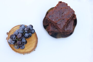 brownie cake with grapes, white background, on wooden slice