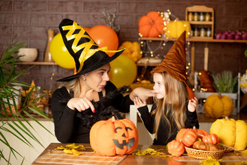 halloween, mom and daughter child in a witch costume with pumpkins and a big spider in a dark kitchen scare each other during the Halloween celebration