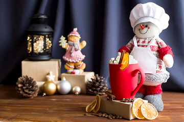A snowman and a red frosted cup with marshmallows and cinnamon on a Christmas background.