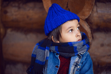 boy child in a blue denim jacket and hat is sitting at a wooden house in autumn