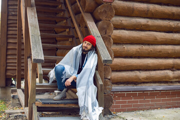 man with a hipster beard in a red knitted hat and a denim jacket is sitting on the stairs